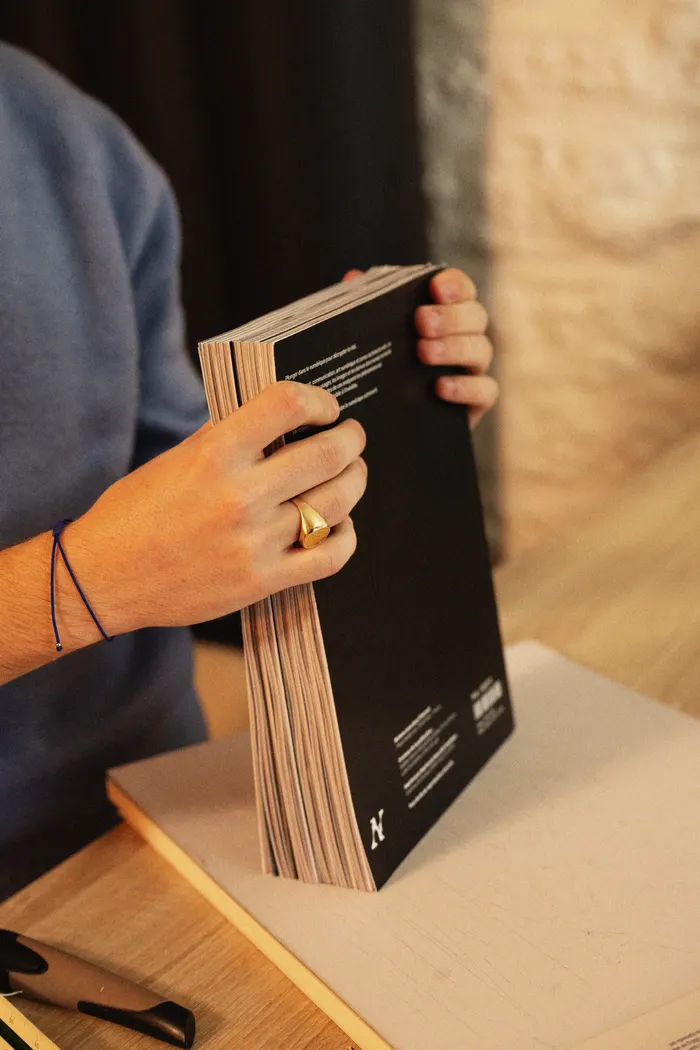 Une pile de numéros du magazine Nichons-nous dans l'internet tenue debout à deux mains, dos carré collé et quatrième de couverture noire.